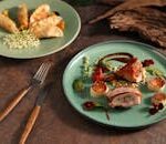 Delicious gourmet goose leg and dumplings plated artistically in a fine dining setting.