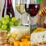 Sophisticated cheese platter with assorted wines, grapes, honey, and nuts.