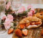 Close-up of delicious croissants with strawberries and cream, accompanied by pink flowers and wine glasses.